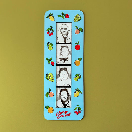Photo booth strip displayed inside vintage fruit magnet frame on fridge